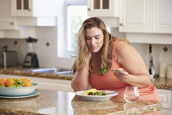 Mulher com excesso de peso comendo refeição saudável na cozinha