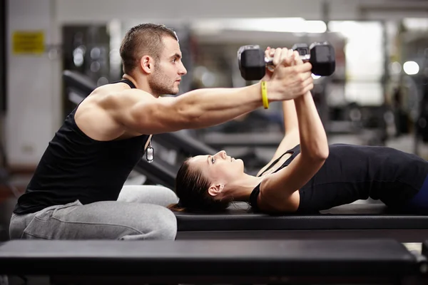 Personal trainer habilidoso ajudando mulher trabalhando com halteres 